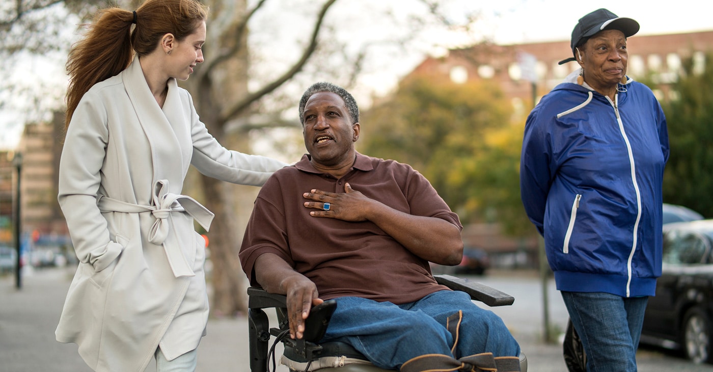 Person in wheelchair with two people strolling in the park