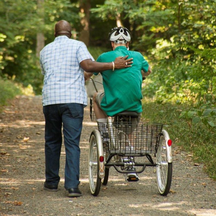 Man helping an older adult ride a bicycle
